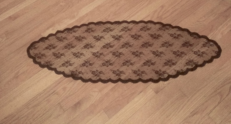 May include: A brown lace table runner with a scalloped edge. The lace has a floral pattern.