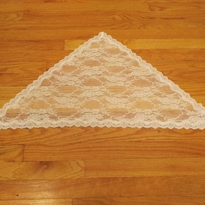 Puede incluir: Un chal triangular de encaje blanco con borde festoneado.