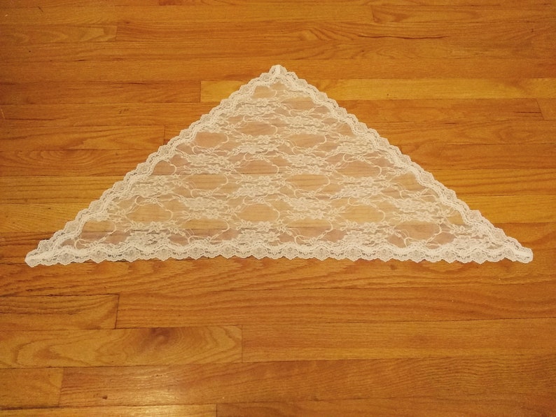Puede incluir: Un chal triangular de encaje blanco con borde festoneado.