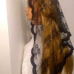 May include: Black lace mantilla with floral pattern and scalloped edges. The mantilla is draped over a mannequin's head and shoulders.