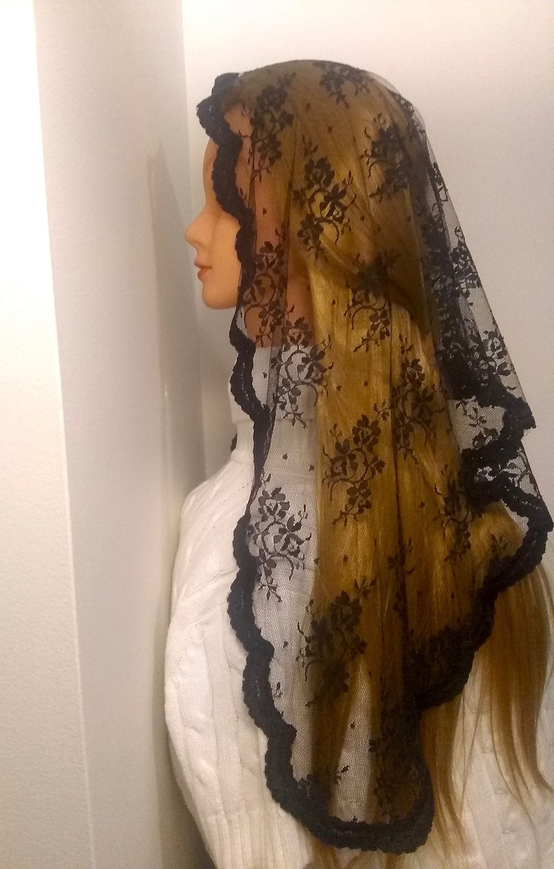 May include: Black lace mantilla with floral pattern and scalloped edges. The mantilla is draped over a mannequin's head and shoulders.