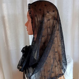 May include: A black lace veil with a scalloped edge. The veil is draped over a mannequin's head and shoulders.