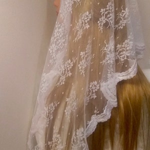 May include: White lace veil with floral pattern. The veil is sheer and has a scalloped edge.