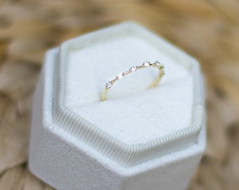 Könnte beinhalten: Ein zarter Goldring mit kleinen, klaren Edelsteinen, die in einer Reihe eingefasst sind. Der Ring wird in einer weißen Ringbox präsentiert.