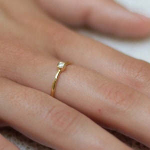 May include: A simple gold band ring with a small, clear gemstone set in the center.