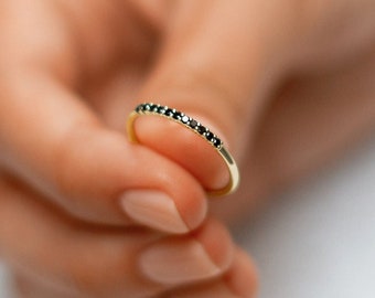 May include: A thin gold band ring with a row of small black diamonds.