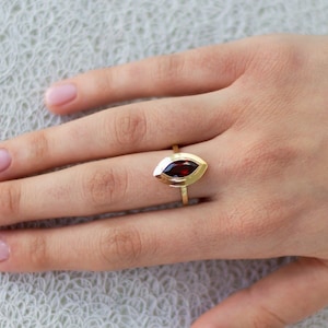 May include: A gold ring with a marquise-shaped red gemstone set in a double-prong setting.