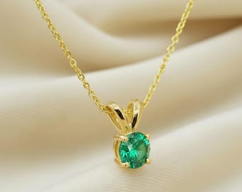 May include: A gold-colored necklace with a round, bright green gemstone pendant. The pendant is held in place by a four-prong setting. The chain is delicate and appears to be made of gold.
