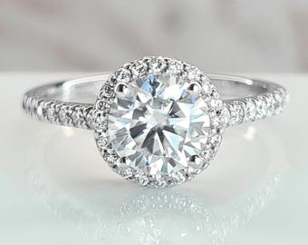May include: A silver engagement ring with a large round center diamond surrounded by a halo of smaller diamonds. The band is also set with smaller diamonds.