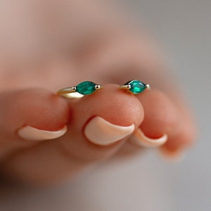 Könnte beinhalten: Zwei goldene Ringe mit smaragdgrünen Edelsteinen. Die Ringe werden an einem Finger gezeigt.