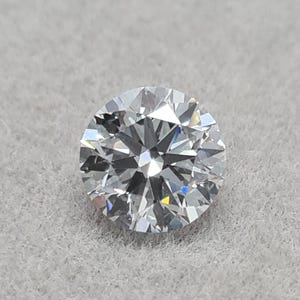 May include: A round-cut diamond with numerous facets, reflecting light. The colorless gemstone is set against a light gray background. The diamond's brilliance is highlighted by the intricate cuts.