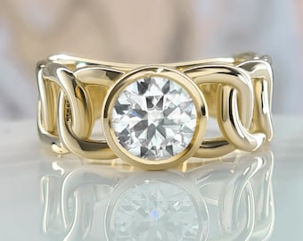 May include: A gold ring with a large, round, bezel-set diamond. The band is made of interlocking loops.