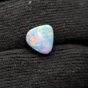 May include: A triangular-shaped opal gemstone featuring a smooth, polished surface with a vibrant play-of-color, displaying iridescent flashes of bright blue, pink, orange, and yellow against a translucent, milky white base color.