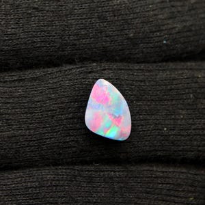 May include: A teardrop-shaped opal gemstone featuring a translucent white base with vibrant flashes of pink, blue, and green iridescence throughout its surface, displaying a polished finish and a smooth, rounded edge profile.