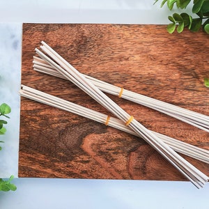 May include: A bundle of natural reed diffuser sticks on a wooden surface. The sticks are tied together with rubber bands.