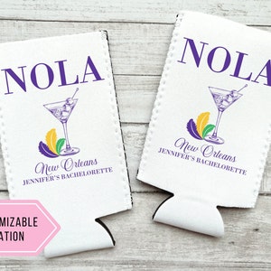 May include: Two white foam can coolers with a purple and gold Mardi Gras theme. The coolers feature the text "NOLA" and "New Orleans Jennifer's Bachelorette".