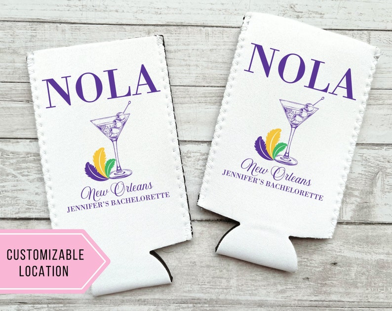 May include: Two white foam can coolers with a purple and gold Mardi Gras theme. The coolers feature the text "NOLA" and "New Orleans Jennifer's Bachelorette".