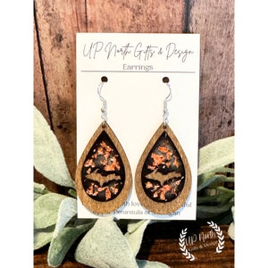 May include: Wooden teardrop earrings with a dark interior, copper-colored accents, and a bat silhouette. The earrings are suspended from silver-colored hooks. The card behind the earrings reads "Up North Gifts & Design" and "Earrings."