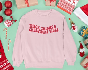 Puede incluir: Sudadera rosa de Navidad con el texto "Thick Thighs & Christmas Vibes" en rojo.