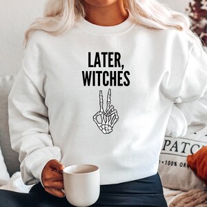 May include: White sweatshirt with the text "Later, Witches" and a black skeleton hand making a peace sign.