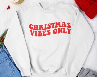 May include: White sweatshirt with red text that says "CHRISTMAS VIBES ONLY" on a white fuzzy background.