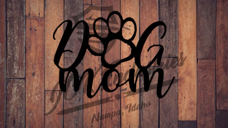 May include: A wooden sign with the words "Dog Mom" in a stylish script font, featuring a paw print design. The sign is set against a rustic, wooden plank background, with the text "Nampa, Idaho" at the bottom.