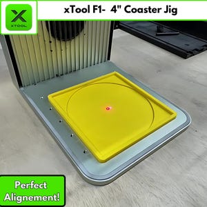 May include: A silver and yellow coaster jig with the text "xTool F1- 4" Coaster Jig" and "Perfect Alignment!". The jig has a yellow square frame with a circular indentation, and a red laser dot. The jig is designed for 4-inch coasters.