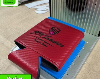 May include: A red carbon fiber-textured koozie jig with the text "JCK Industries Nampa, Idaho" and a logo. The jig is on a blue base, with the text "xTool F1- Koozie Jig" above. The words "Perfect Alignment!" are in a green box.