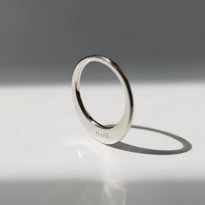 Puede incluir: Un anillo de plata con una forma redondeada y lisa. El anillo está inscrito con la palabra "MOU".