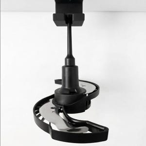 Può includere: Utensile da cucina nero con una lama curva e un manico. Il dispositivo è montato su una superficie bianca. La lama è argentata e il resto del dispositivo è nero. L'apparecchio sembra essere un affettatrice.