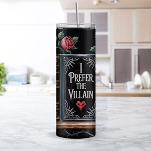 Puede incluir: Un vaso de acero inoxidable negro con un dise&ntilde;o de libro con una rosa y el texto "I Prefer the Villain" con un coraz&oacute;n.