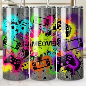 Puede incluir: Un vaso de acero inoxidable con un diseño de graffiti colorido con mandos de juego y el texto "GAME OVER". El diseño incluye salpicaduras de verde neón, rosa, azul y morado sobre un fondo gris.