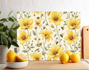 Op de afbeelding: Rechthoekige decoratieve snijplank met een bloemenpatroon van gele bloemen en bijen op een crèmekleurige achtergrond. De plank is gemaakt van een duurzaam materiaal en is geschikt voor gebruik in de keuken. Citroenen in een witte kom staan op de voorgrond.