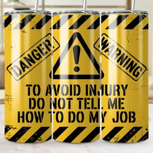 Peut inclure: Gobelet jaune avec des rayures diagonales noires et les mots "DANGER" et "WARNING". Le gobelet porte un triangle noir avec un point d'exclamation et le texte "TO AVOID INJURY DO NOT TELL ME HOW TO DO MY JOB".