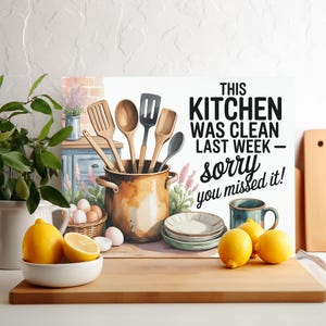 May include: A kitchen-themed print with the text "This Kitchen Was Clean Last Week - Sorry You Missed It!". The image features wooden utensils in a pot, lemons, eggs, and plates, creating a rustic, homey feel.
