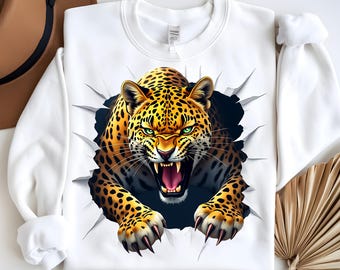 May include: White sweatshirt featuring a detailed illustration of a leopard bursting through a torn surface. The leopard has a fierce expression with green eyes and an open mouth, showcasing its teeth. The design is bold and eye-catching.