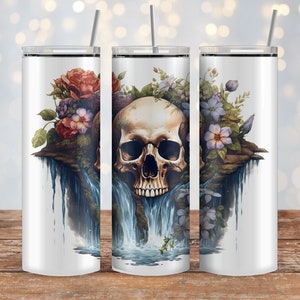 May include: A white, stainless steel tumbler with a skull and floral design. The skull is centered, surrounded by red, purple, and blue flowers, with a waterfall effect. A silver straw is inserted in the lid. The tumbler is on a wooden surface.
