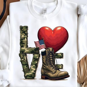 May include: White sweatshirt with a camouflage print of the word "LOVE" with a red heart and an American flag above the "O" and a brown military boot on the right side of the "E".