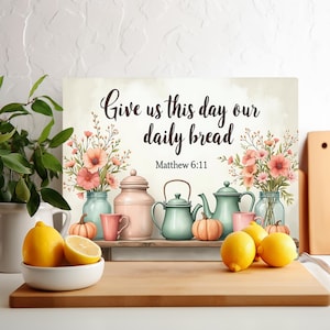 Może przedstawiać: Dekoracyjny nadruk kuchenny z tekstem "Give us this day our daily bread" i "Matthew 6:11". Nadruk przedstawia kompozycje kwiatowe, czajniki, dynie i cytryny. Paleta kolorów obejmuje róż, niebieski i żółty.