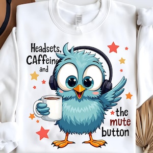 May include: White sweatshirt featuring a cartoon blue bird wearing headphones and holding a coffee mug. Text on the shirt reads "Headsets, Caffeine and the mute button". Orange and yellow stars are scattered around the bird.