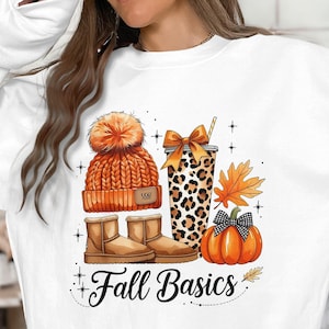 Puede incluir: Sudadera blanca con un diseño de temática otoñal. El diseño incluye un gorro naranja de punto, botas marrones, una taza con estampado de leopardo, una calabaza y el texto "Fall Basics."