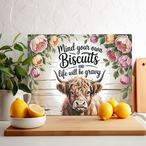 Może przedstawiać: Rustykalny drewniany znak z krową szkocką i kwiatowymi akcentami. Na znaku widnieje napis "Mind your own Biscuits and life will be gravy."