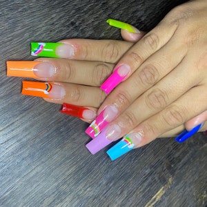 May include: Close-up of hands with long, colorful, and decorated acrylic nails. The nails are painted in various colors, including orange, pink, blue, green, and red. Each nail features a rainbow design with a white cloud.