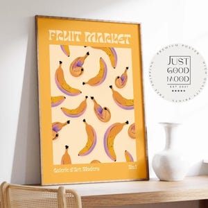 Könnte beinhalten: Ein gerahmtes Poster mit gelbem Rand zeigt ein sich wiederholendes Muster aus Bananen in Gelb- und Lilatönen. Die Worte "FRUIT MARKET" stehen oben. Der untere Teil des Posters lautet "Galerie d'Art Modern".