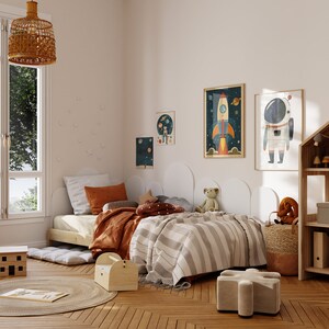 May include: A white twin-sized bed with a brown and orange striped blanket and a brown and orange patterned pillow. The bed is in a room with a white wall and a window with a view of trees. There are several framed pictures on the wall, including one of a rocket ship and another of an astronaut. There is a wooden toy shelf in the corner of the room.