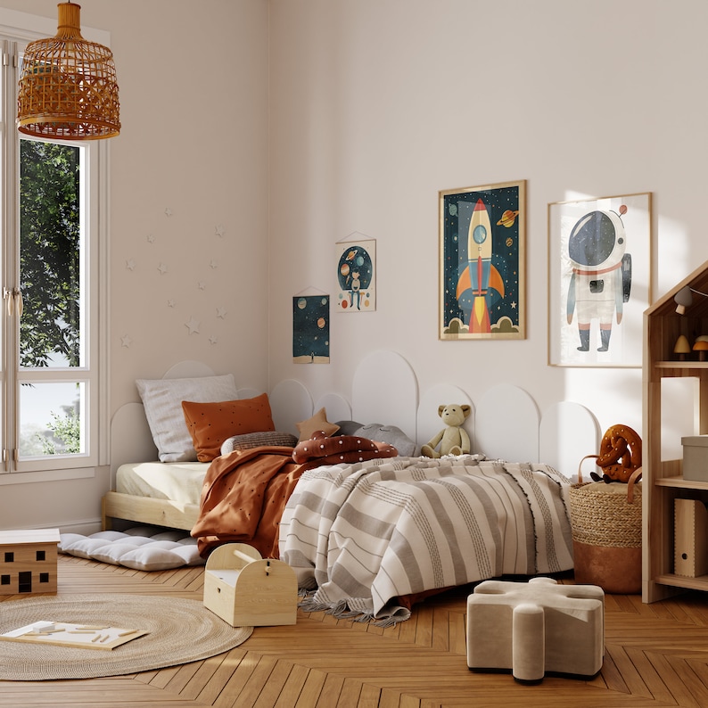 May include: A white twin-sized bed with a brown and orange striped blanket and a brown and orange patterned pillow. The bed is in a room with a white wall and a window with a view of trees. There are several framed pictures on the wall, including one of a rocket ship and another of an astronaut. There is a wooden toy shelf in the corner of the room.