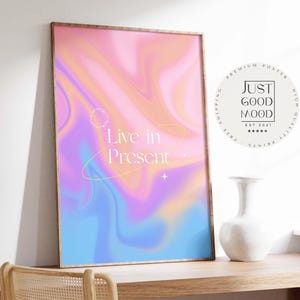 Puede incluir: Un póster enmarcado con un diseño abstracto en tonos rosa, naranja, azul y morado. El texto "Live in Present" se muestra en blanco, con una estrella y un diseño circular. El póster está etiquetado como "Just Good Mood".