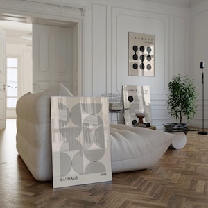 Puede incluir: Una impresi&oacute;n geom&eacute;trica en blanco y negro con el texto "BAUHAUS 1919" sobre un fondo blanco. La impresi&oacute;n est&aacute; enmarcada y colgada en una pared blanca en una sala de estar moderna.