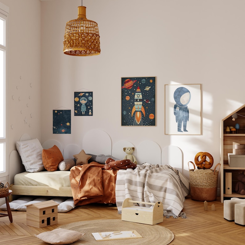 May include: A child's bedroom featuring a white bed with a brown and white blanket and a brown and white rug. Three framed prints adorn the wall, one depicting a rocket ship, another an astronaut, and the third a child in a spacesuit. A wooden toy house sits on the floor, alongside a brown wicker basket containing a pretzel, and a wooden shelf stocked with toys.