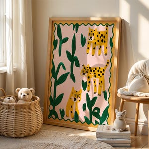 May include: A framed print with a pink background and green leaves. Three yellow and black leopards are depicted in the print. The print is hanging on a wall in a room with a wicker basket and stuffed animals.